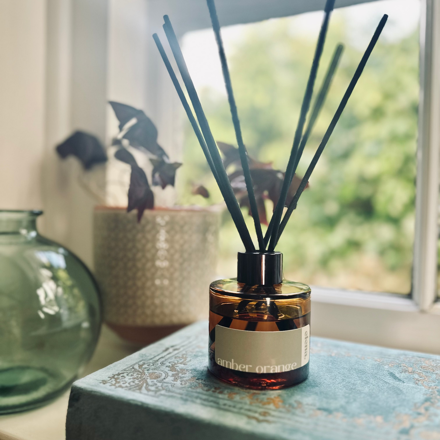 elena london reed diffuser with sticks in amber orange fragrance styled by a window