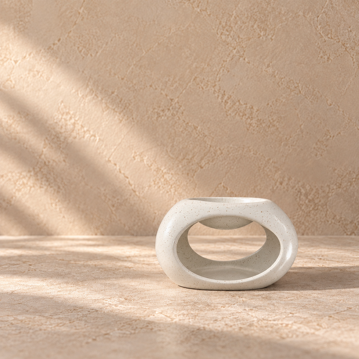 A minimalist off-white ceramic wax  melt burner with a textured finish, set on a matching stone surface against a textured beige wall with soft leaf shadows.
