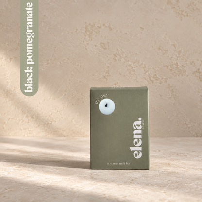 a sage green box for the elena London wax melt bar labelled 'black pomegranate', standing on a textured beige surface with soft shadows. 