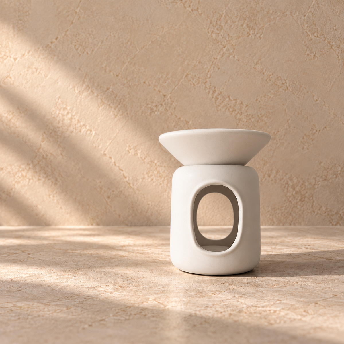 A minimalist white ceramic wax melt burner with a wide shallow saucer and cylindrical base featuring an oval cutout, set on a textured beige stone surface against a matching beige wall with soft diagonal shadows.
