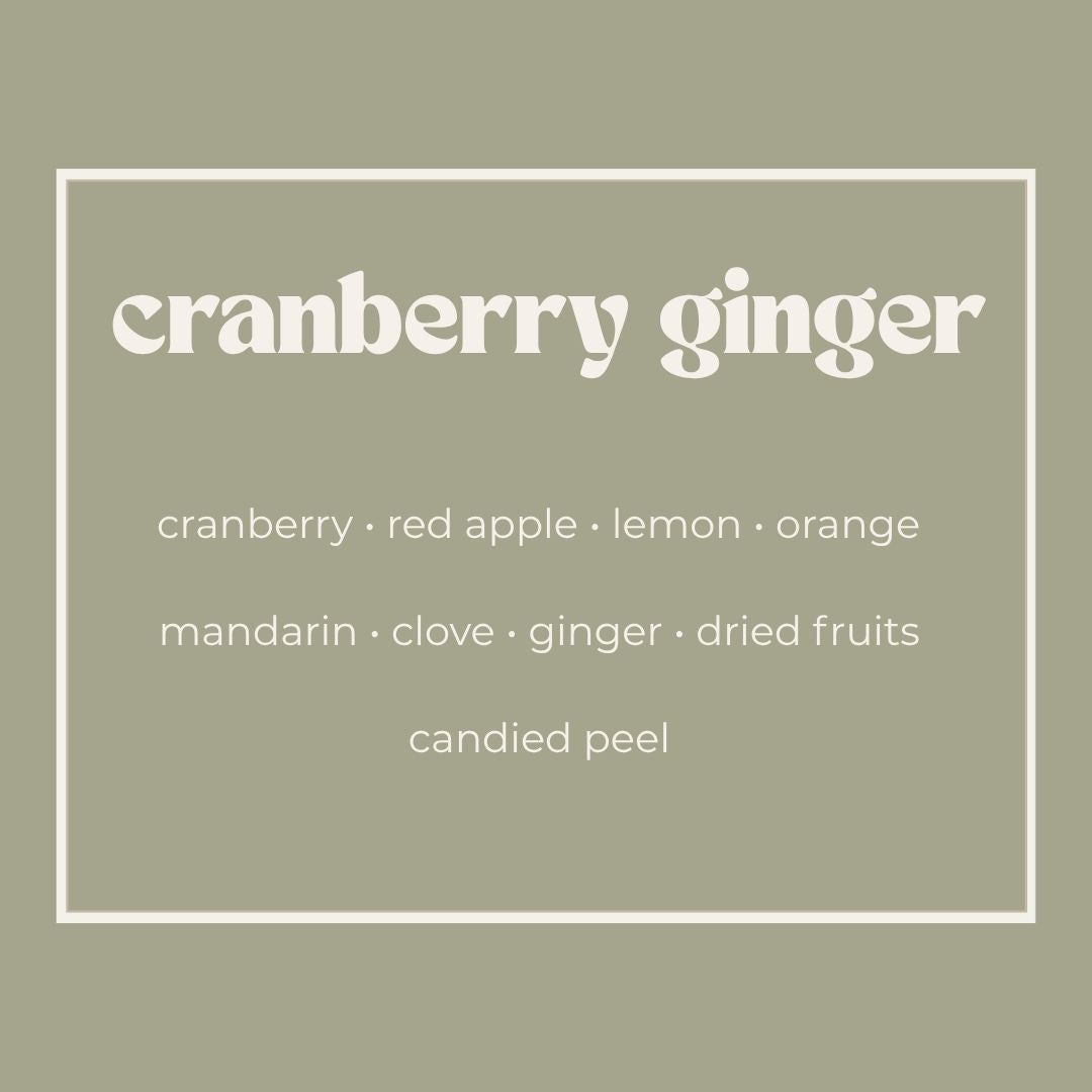 A square graphic with a muted sage green background and a thin white border. The text reads 'cranberry ginger' in large white serif letters, with smaller white text below listing scent notes: cranberry, red apple, lemon, orange, mandarin, clove, ginger, dried fruits, and candied peel.