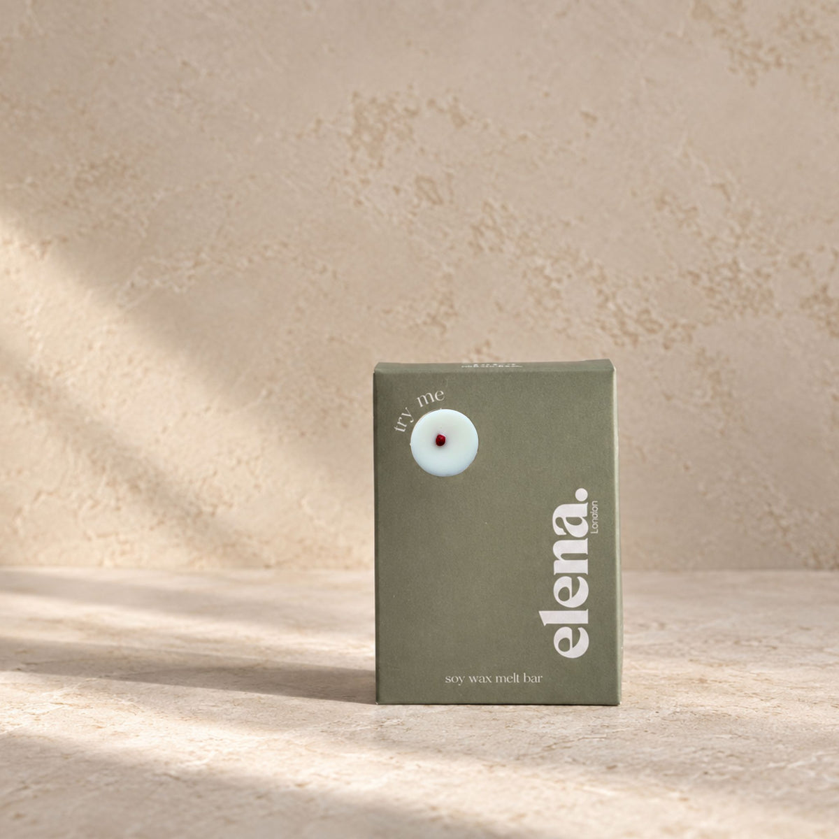 An elena London cranbery ginger soy wax melt Bar stands on a light stone surface against a textured beige wall, with soft diagonal shadows across the scene.