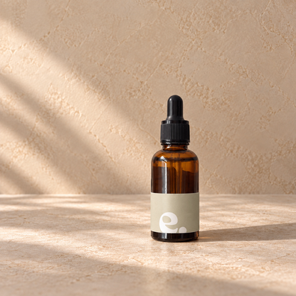 An car diffuser refill amber glass dropper bottle with a black dropper cap and a light beige label, standing on a stone-like surface against a textured beige wall with soft diagonal shadows.