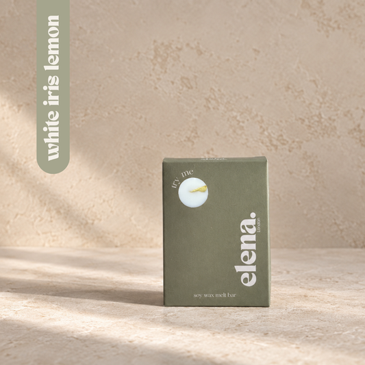 a sage green box for the elena London wax melt bar labelled 'white iris lemon' with a dried botanical inside. set against a textured beige background with soft shadows.